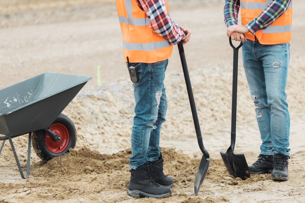 Two builders are leaning on shovels on the road construction site